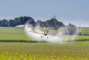 A crop duster applies chemicals to a field of vegetation.